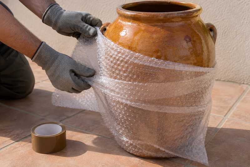 Mains gantées enveloppant une jarre en terre cuite dans du papier bulle