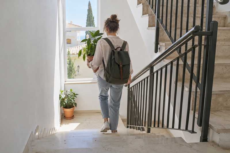 Jeune locataire descendant l'escalier d'une résidence avec un sac et une plante