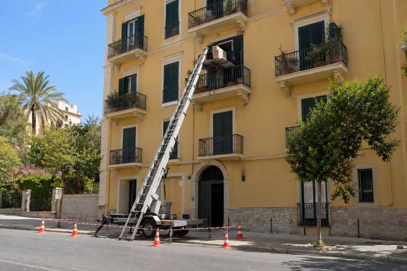 Monte-meuble dressé contre une façade ocre, trottoir balisé de cônes